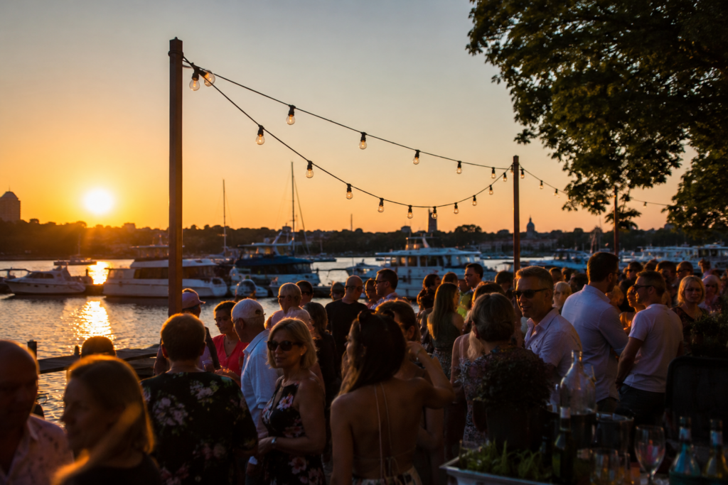 Schlager Potsdam in sommerlicher Marina-Atmosphäre: Menschen feiern bei Sonnenuntergang am Wasser mit Booten im Hintergrund.