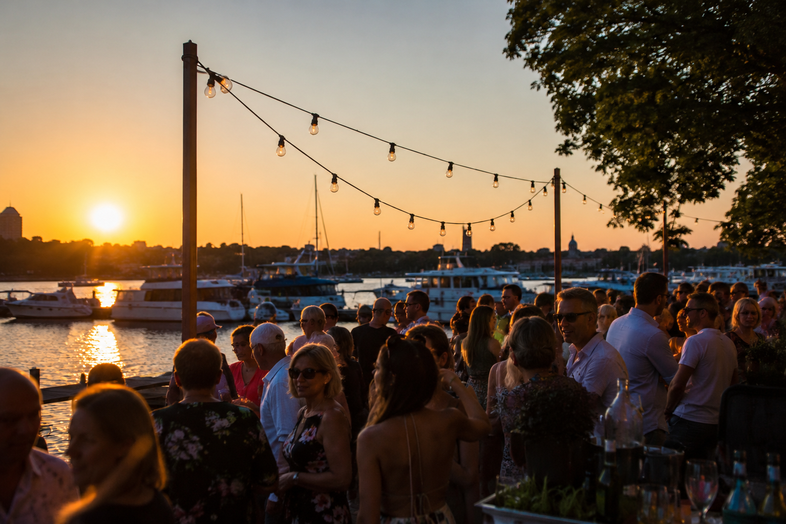 Schlager Potsdam in sommerlicher Marina-Atmosphäre: Menschen feiern bei Sonnenuntergang am Wasser mit Booten im Hintergrund.