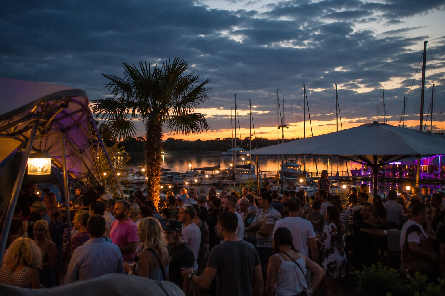 Menschen feiern an einer Marina am Wasser während der Abenddämmerung. Die Atmosphäre der Schlagerparty am Tiefen See Potsdam spiegelt sich in Lichtern, Booten und sommerlichem Himmel wider.